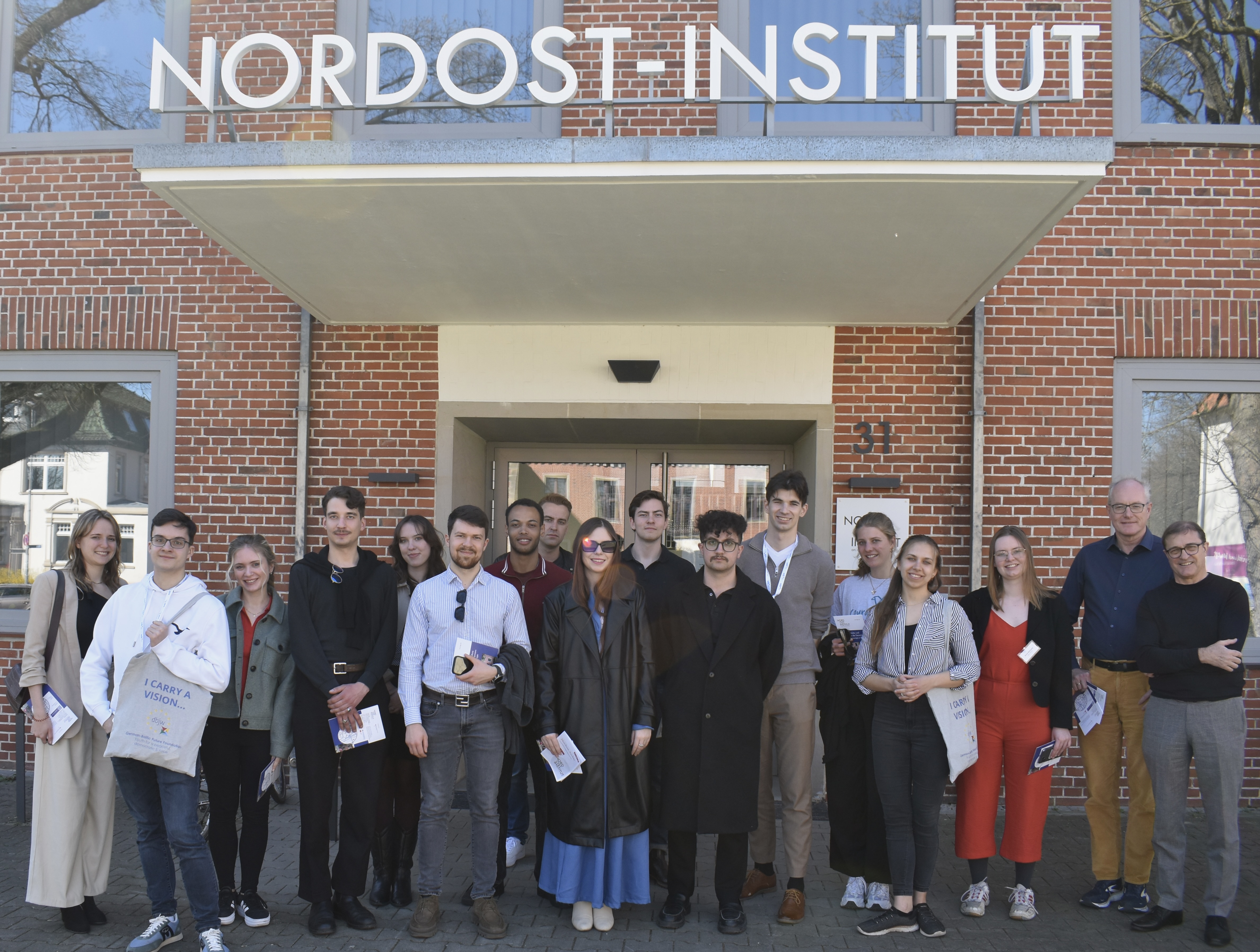 Das Bild zeigt den Eingang des Nordost-Instituts und davor steht eine Gruppe von Menschen, die sich das Institut mit Herrn Henning angeschaut haben.