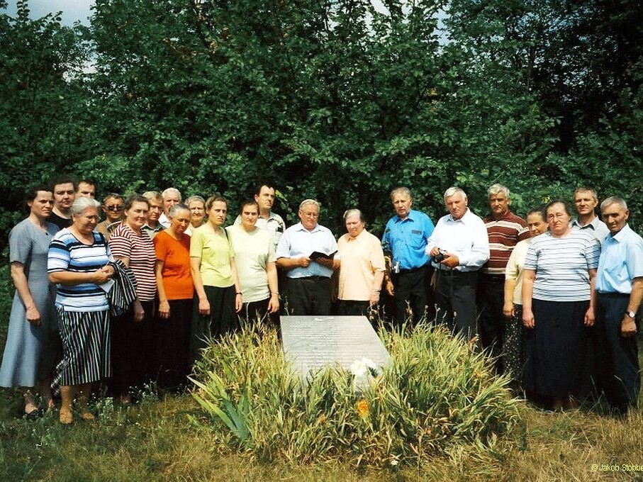 Eine Gruppe von Mennoniten aus Warendorf (Deutschland) vor einem Denkmal für die Opfer der Machnos-Pogrome in Novo-Petrovka (Eichenfeld), Ukraine. Das Foto stammt von Jakob Stobbe, 2005.